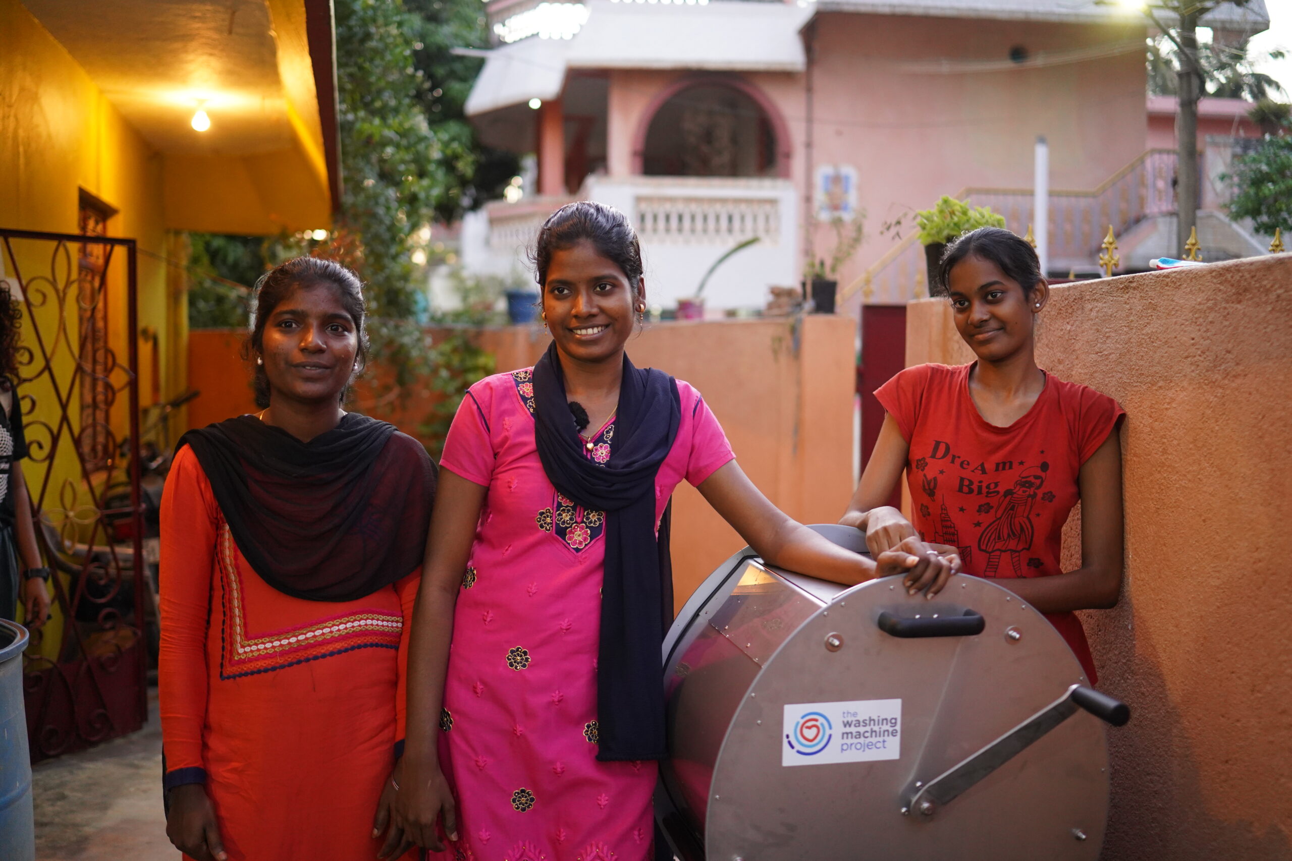 Three women in India pose with The Divya manual washing machine