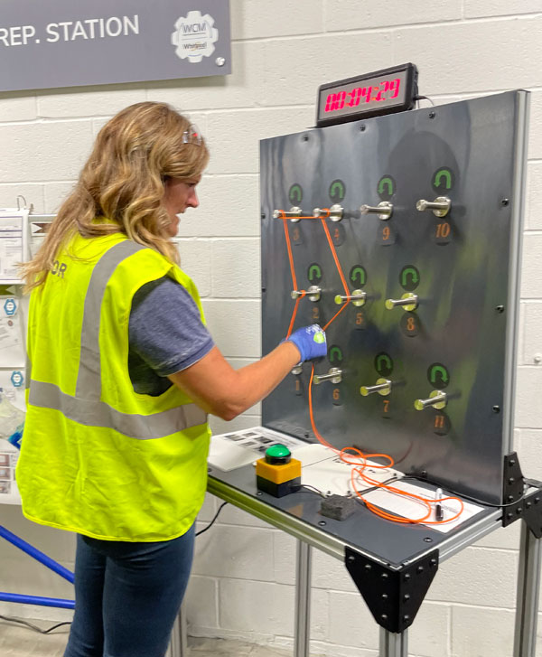 Ottawa female teacher with blonde hair, safety vest, protective gloves, wearing jeans trying her hand at a circuit board during the Whirlpool manufacturing bootcamp for educators