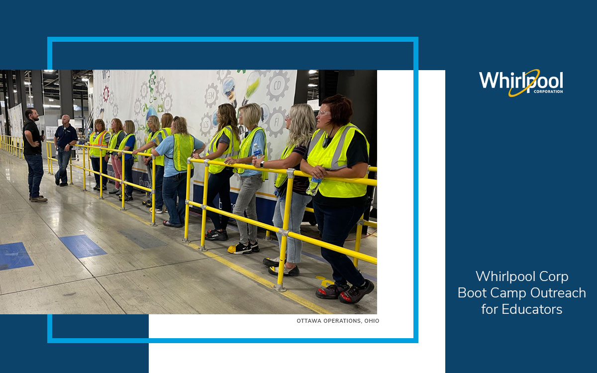 10 female educators wearing bright yellow safety vests and protective coverings on their shoes line up at a yellow railing to listen to two manufacturing leaders at Whirlpool Corp.